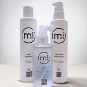 Trzy wegańskie kosmetyki marki Mi and I: wzmacniający tonik do skóry głowy Scalp Tonic, delikatny szampon Soft Shampoo oraz nawilżająca odżywka Rinse Conditioner.