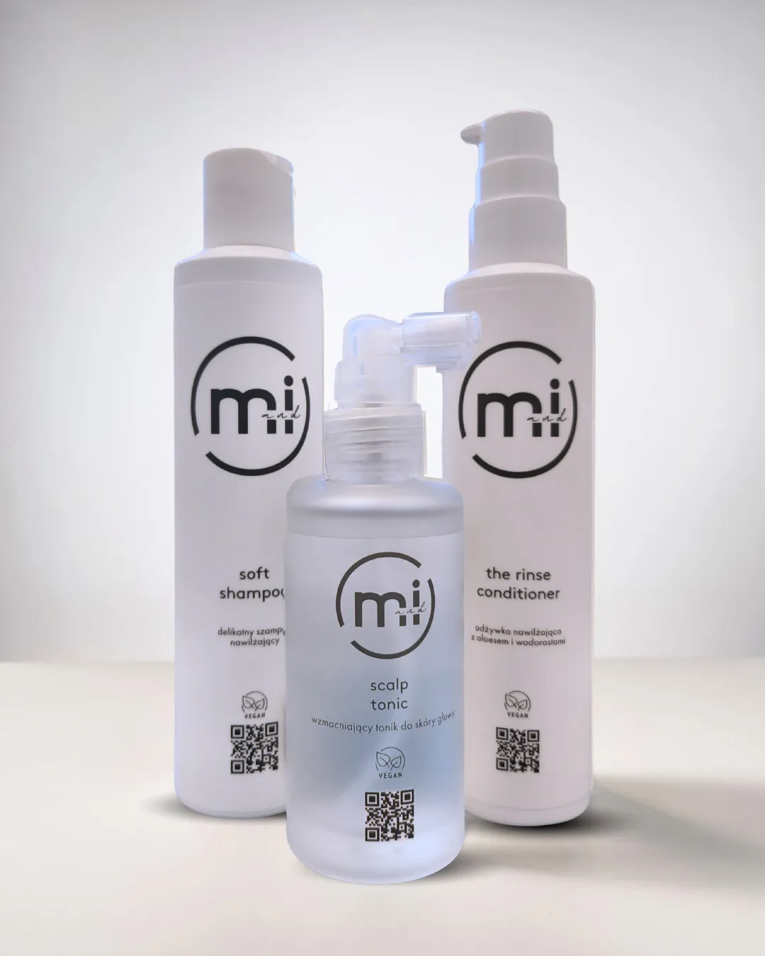 Trzy wegańskie kosmetyki marki Mi and I: wzmacniający tonik do skóry głowy Scalp Tonic, delikatny szampon Soft Shampoo oraz nawilżająca odżywka Rinse Conditioner.